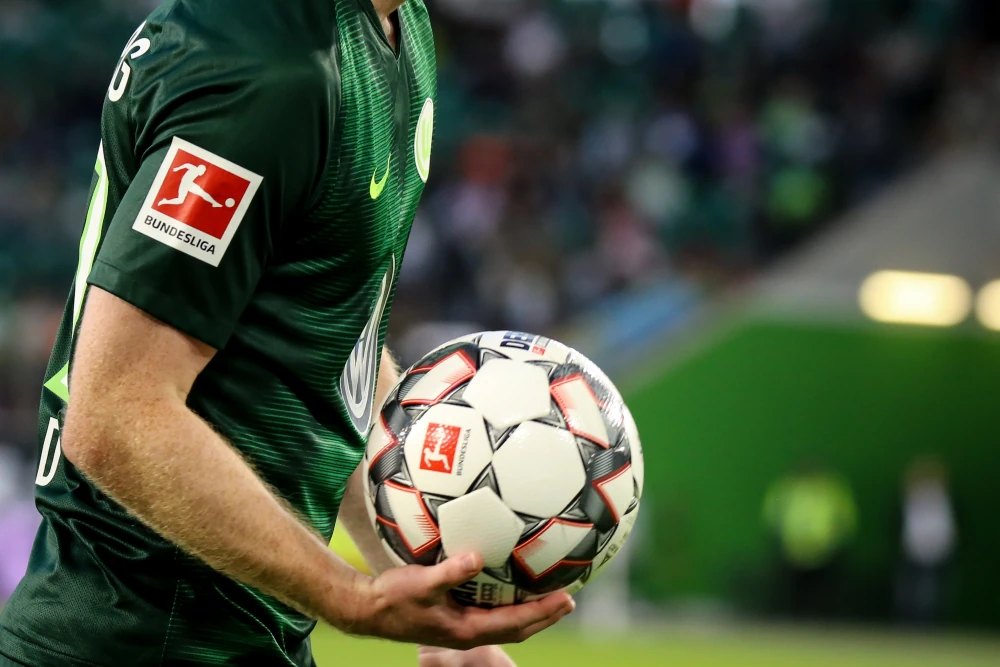 Bundesliga-logga på spelares tröja och fotbollen i hans händer