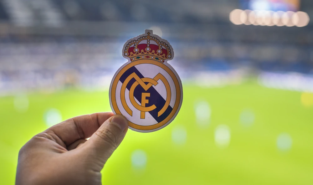 Real Madrid-logga med en fotbollsplan i bakgrunden