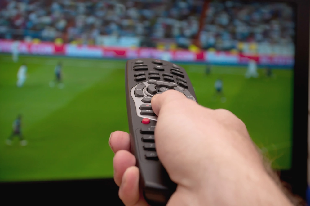 Fjärrkontroll som pekar mot en TV som visar fotboll